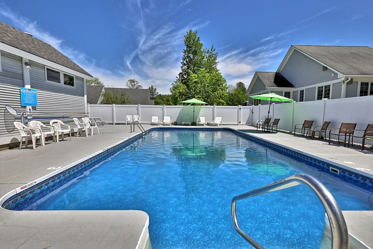 A serene outdoor pool scene featuring a sparkling saltwater pool bordered by lush trees, green umbrellas, and inviting lounge chairs. The setting feels leisurely and social—ideal for relaxing swims or gathering with friends between adventures.