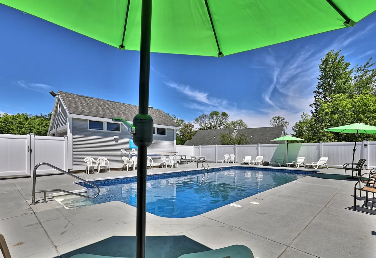 This image features an inviting outdoor swimming pool area with green umbrellas, lounge chairs, and plenty of space for socializing or relaxing. The open-air setting suggests leisure and community, with a lively yet comfortable vibe that can be enjoyed during both the day and evening.