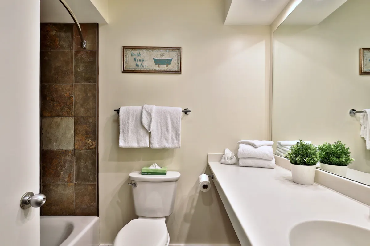 A tranquil bathroom scene featuring a bathtub, a clean vanity, a decorative sign, plush towels, and a green plant. The mood is refreshing and serene, ideal for self-care routines after a day outdoors.