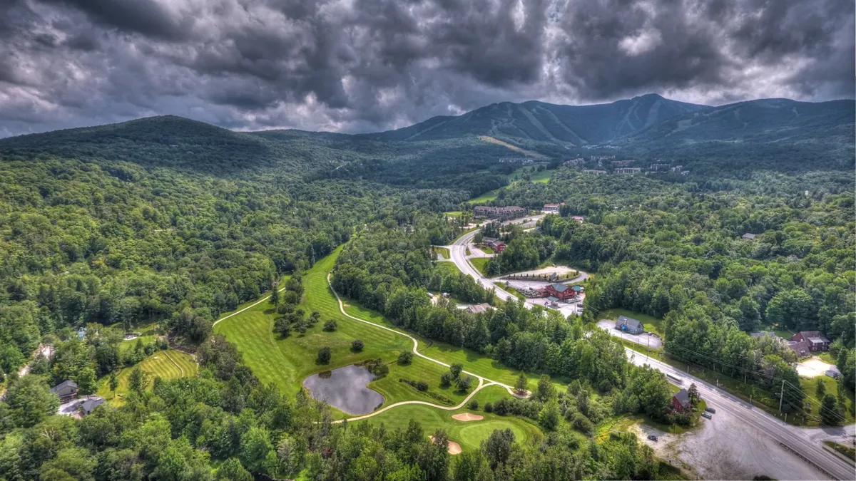 This panoramic view captures Vermont’s lush green landscape, a winding road, a golf course, a tranquil pond, and distant mountain peaks. The scene exudes tranquility and adventure, connecting visitors to hiking, golfing, and the stunning natural surroundings described in the section.